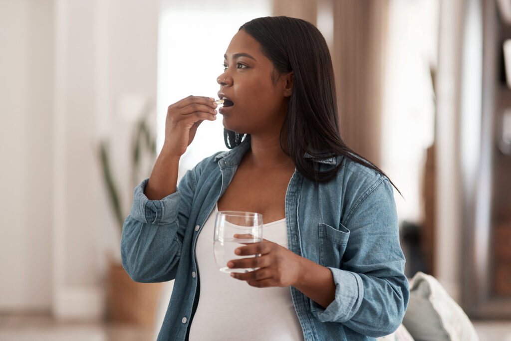 Image of a pregnant woman taking vitamins and supplement product at home.